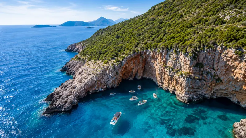 Aerial view of speedboats moored in a turquoise cove below cliffs near the Blue Cave